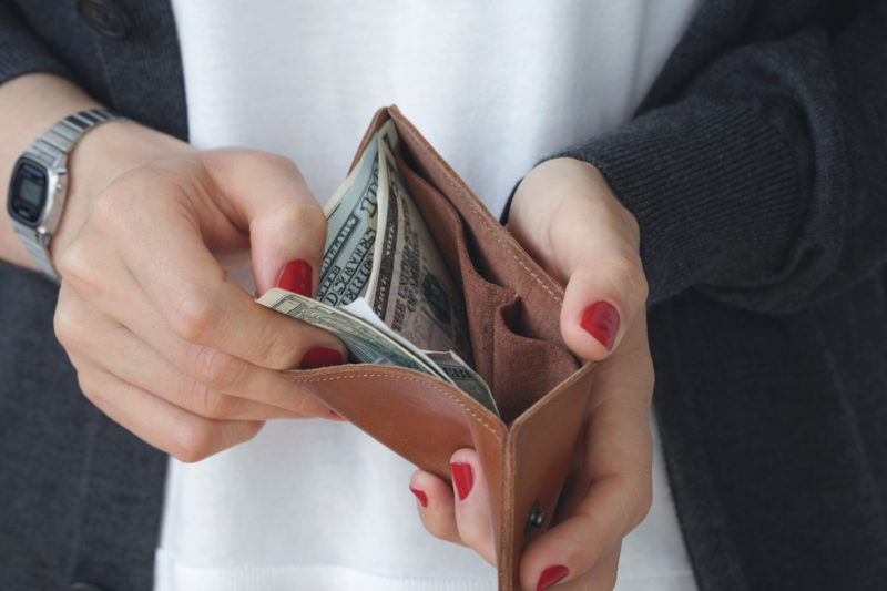 Hands holding an open leather orange slim purse with cash dollars.